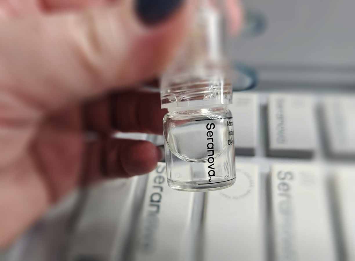 Nahaufnahme eines Seranova-Serumfläschchens mit transparenter Flüssigkeit, wird von einer Hand gehalten.